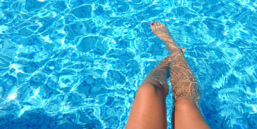 persona-con-los-pies-en-una-piscina-de-agua-cristalina